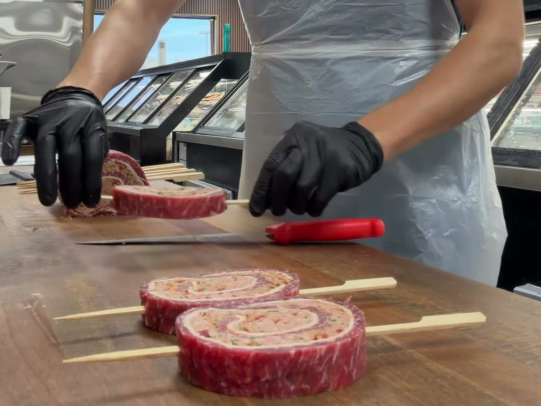 Hands preparing beef skewers at the butcher’s block